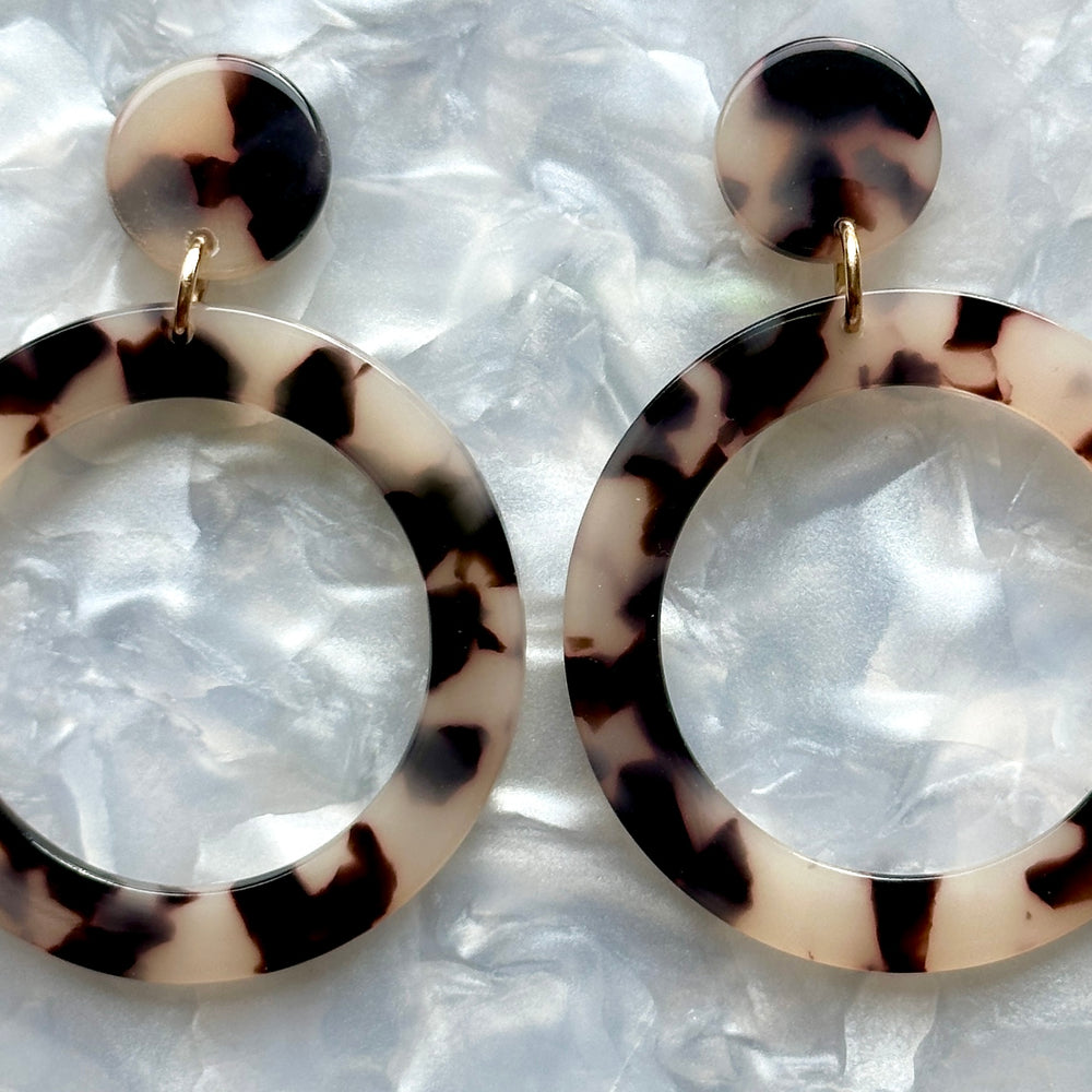 Close up of Acrylic open circle drop earrings in black and white tortoise