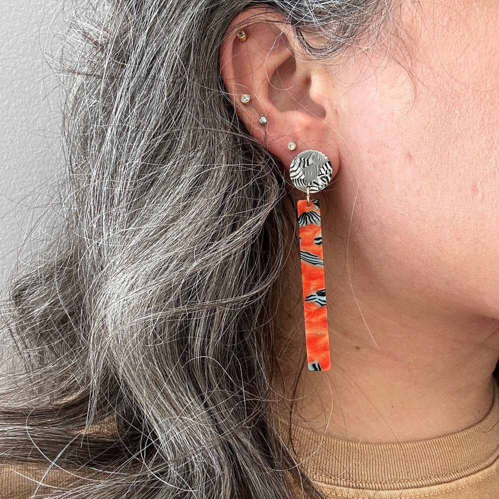 woman wearing acrylic Matchstick Drop Earrings in Safari Sunrise orange, black and white