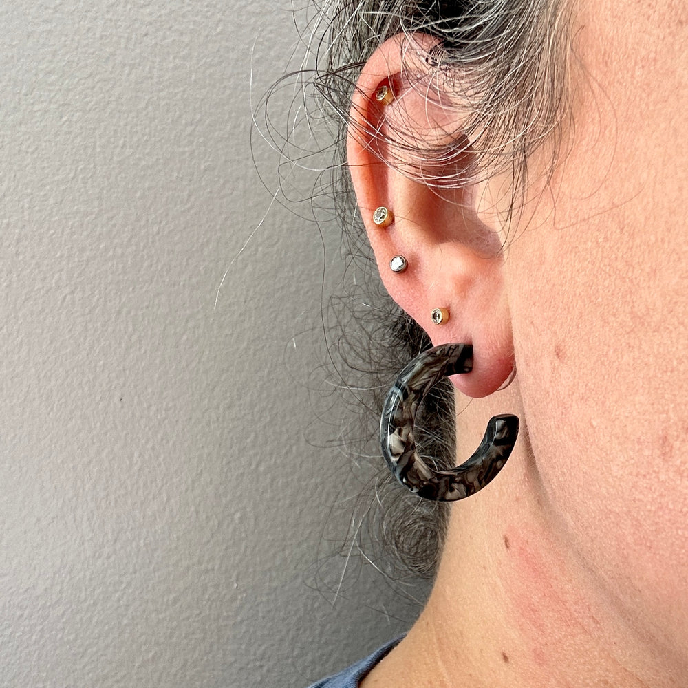 Women wearing mini acrylic hoop earrings in a mix of black, gray, and white 